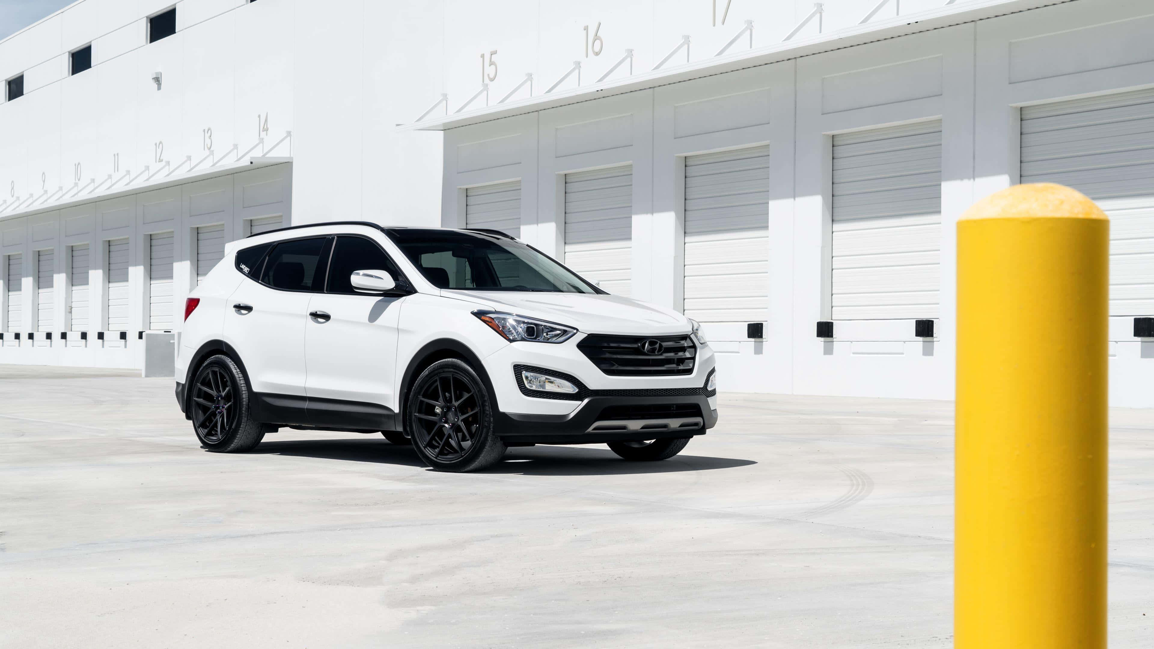 Hyundai Santa Fe 桌布 壁紙 — 一輛時尚的白色現代Santa Fe SUV，配黑色輪圈，停在白色工業建築前，光線明亮。