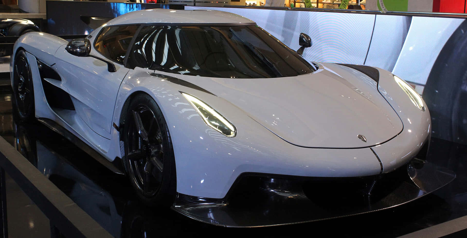  壁紙 — 一輛時尚的白色Koenigsegg超跑在車展的亮黑色展示台上，在明亮燈光下閃閃發光。