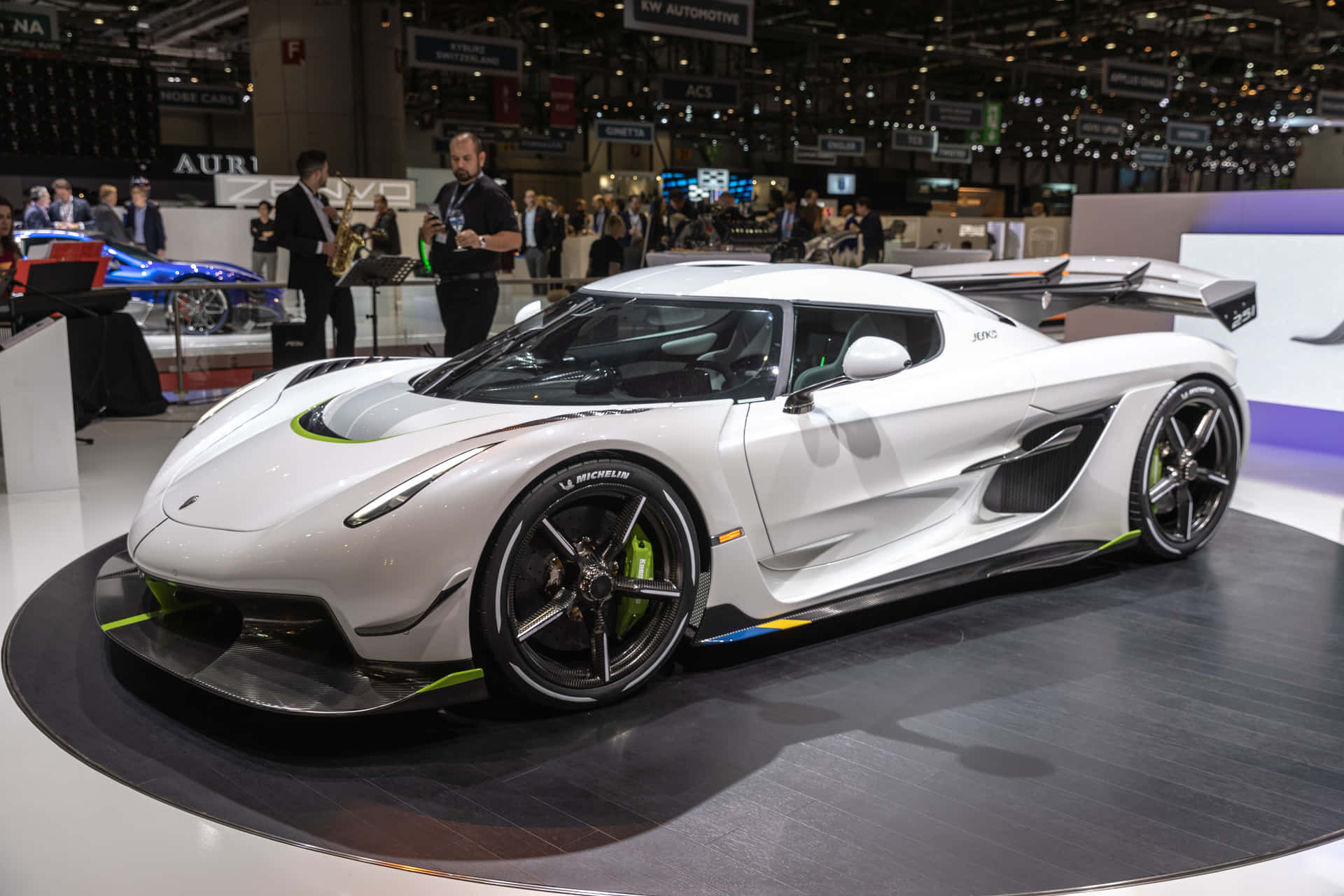 壁紙 — 一輛帶有綠色點綴的時尚白色Koenigsegg超跑在繁忙的車展旋轉平台上展示。