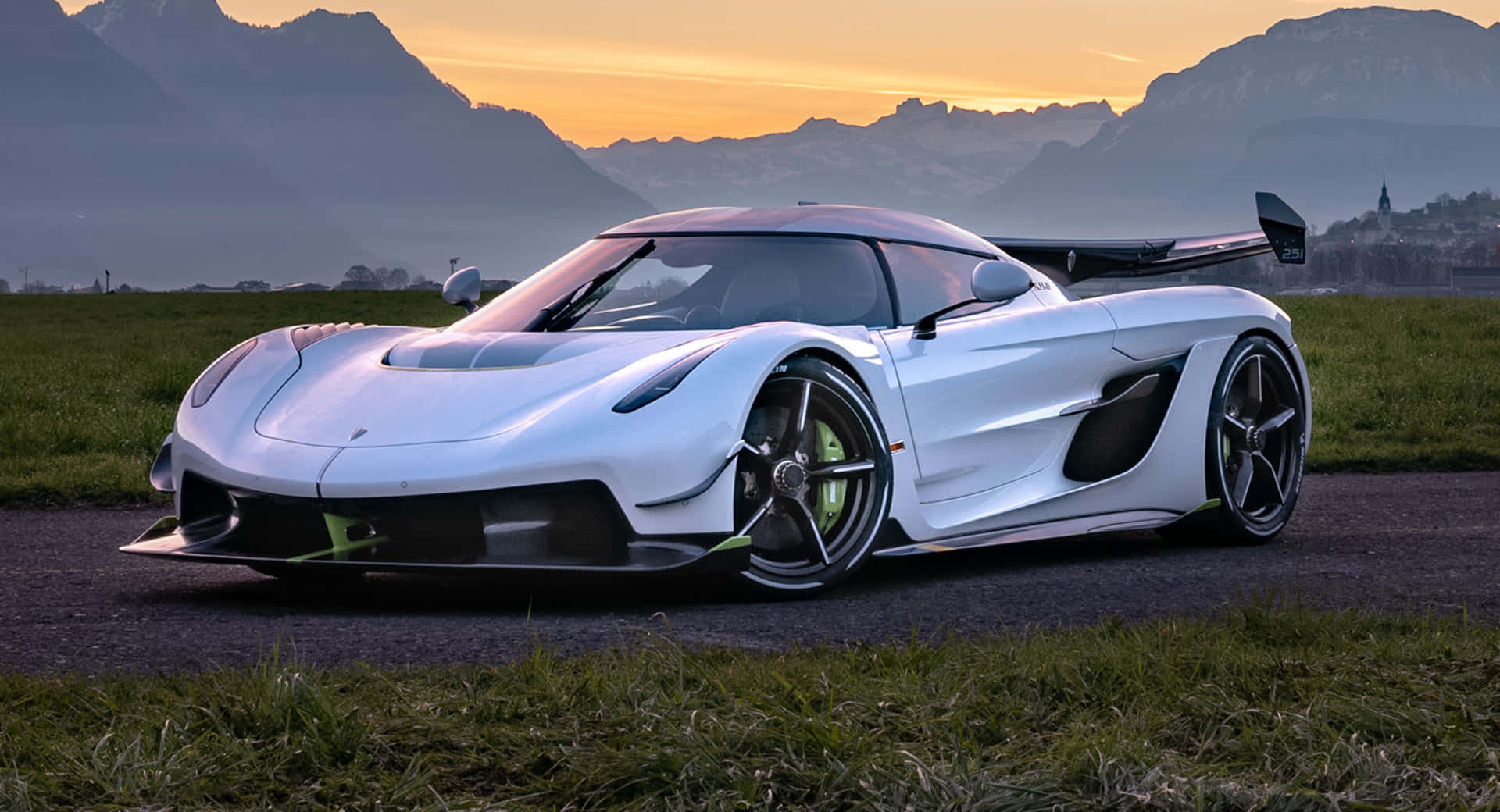  壁紙 — 一架時尚的白色 Koenigsegg 超級跑車，帶有青檸綠色點綴，在日落時分停泊在碎石路上，背景是山區地形。