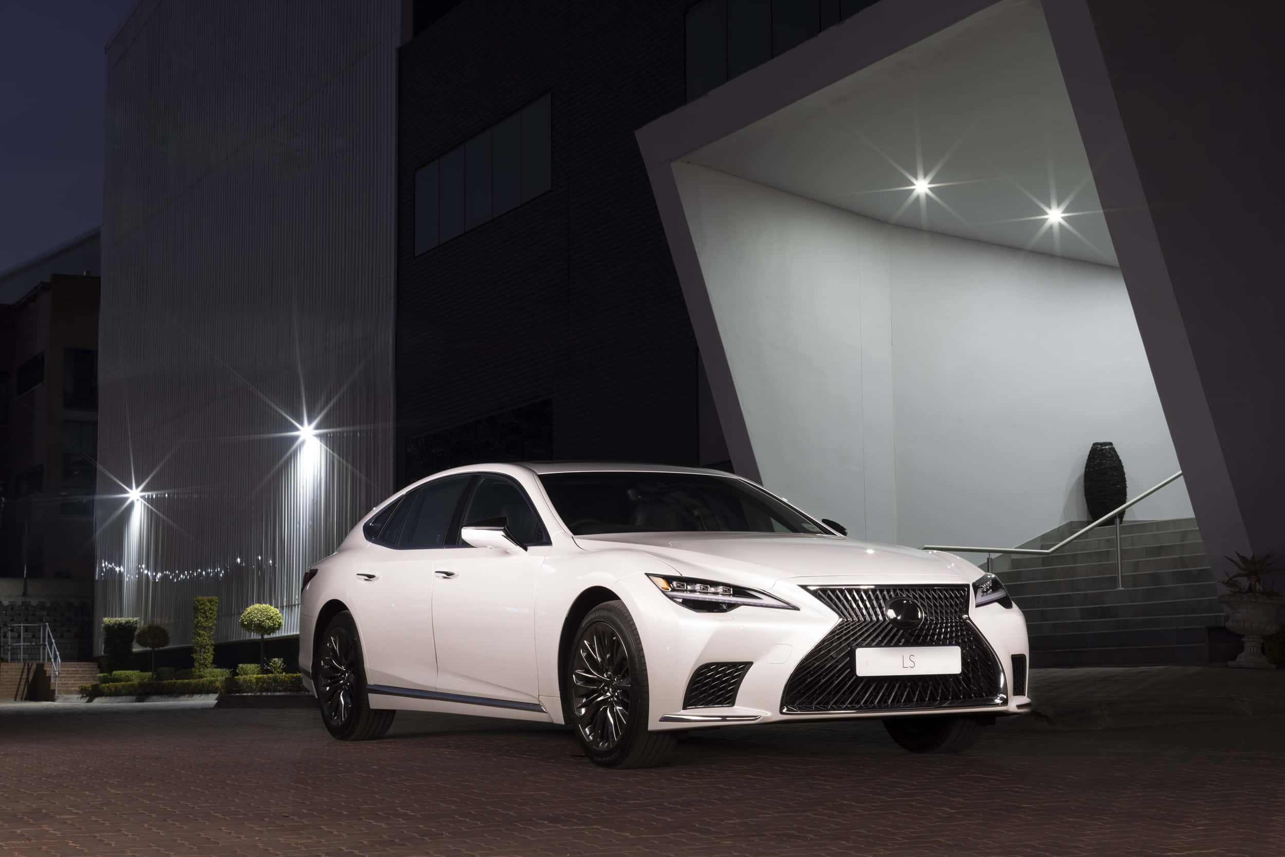 Lexus Ls 500 桌布 壁紙 — 一輛時尚的白色Lexus LS轎車在夜燈下閃耀，以現代建築為背景。