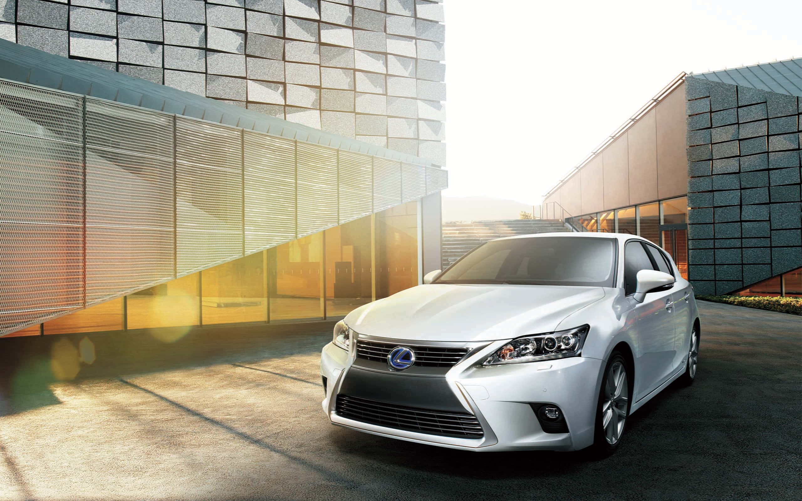 Lexus Ct 200h 桌布 壁紙 — 一輛時尚的白色Lexus房車在金色陽光下閃耀，位於現代幾何建築之間，建築物帶有反光玻璃外牆。