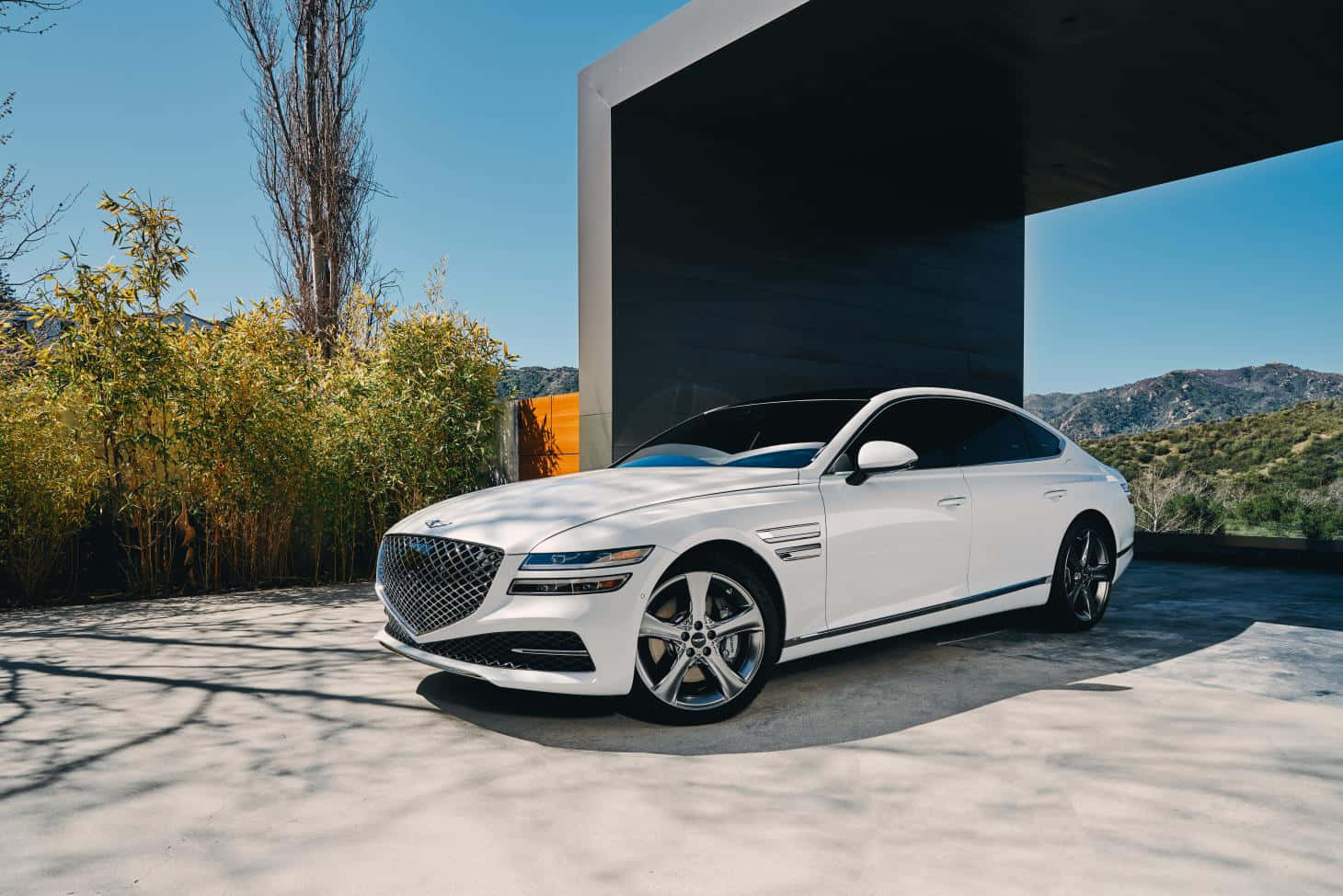 Genesis G80 桌布 壁紙 — 一輛時尚的白色豪華轎車停泊在現代混凝土簷篷下，背景有山脈和金黃色的樹葉。