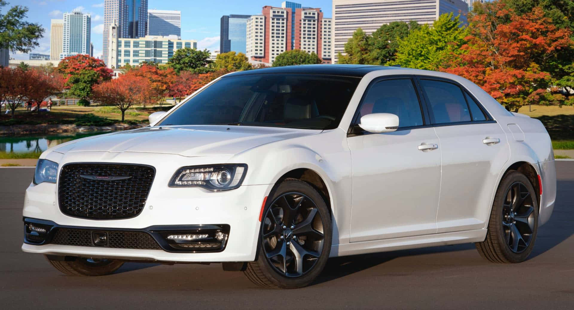 Chrysler 300 桌布 壁紙 — 一輛時尚的白色豪華轎車配黑色輪圈，停在秋樹和城市天際線前，天空清澈湛藍。