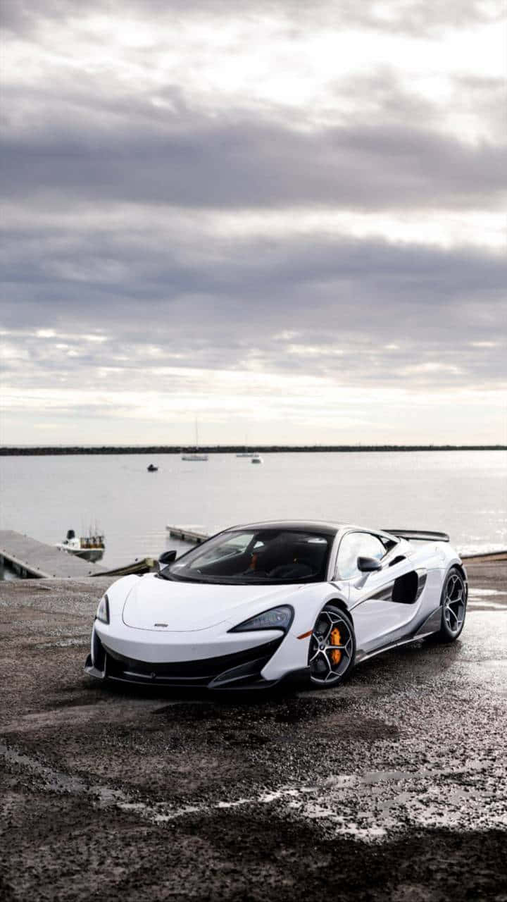 Mclaren 600lt 桌布 壁紙 — 一架時尚的白色McLaren跑車停泊在潮濕的碼頭上，旁邊是平靜的水面，天空多雲。