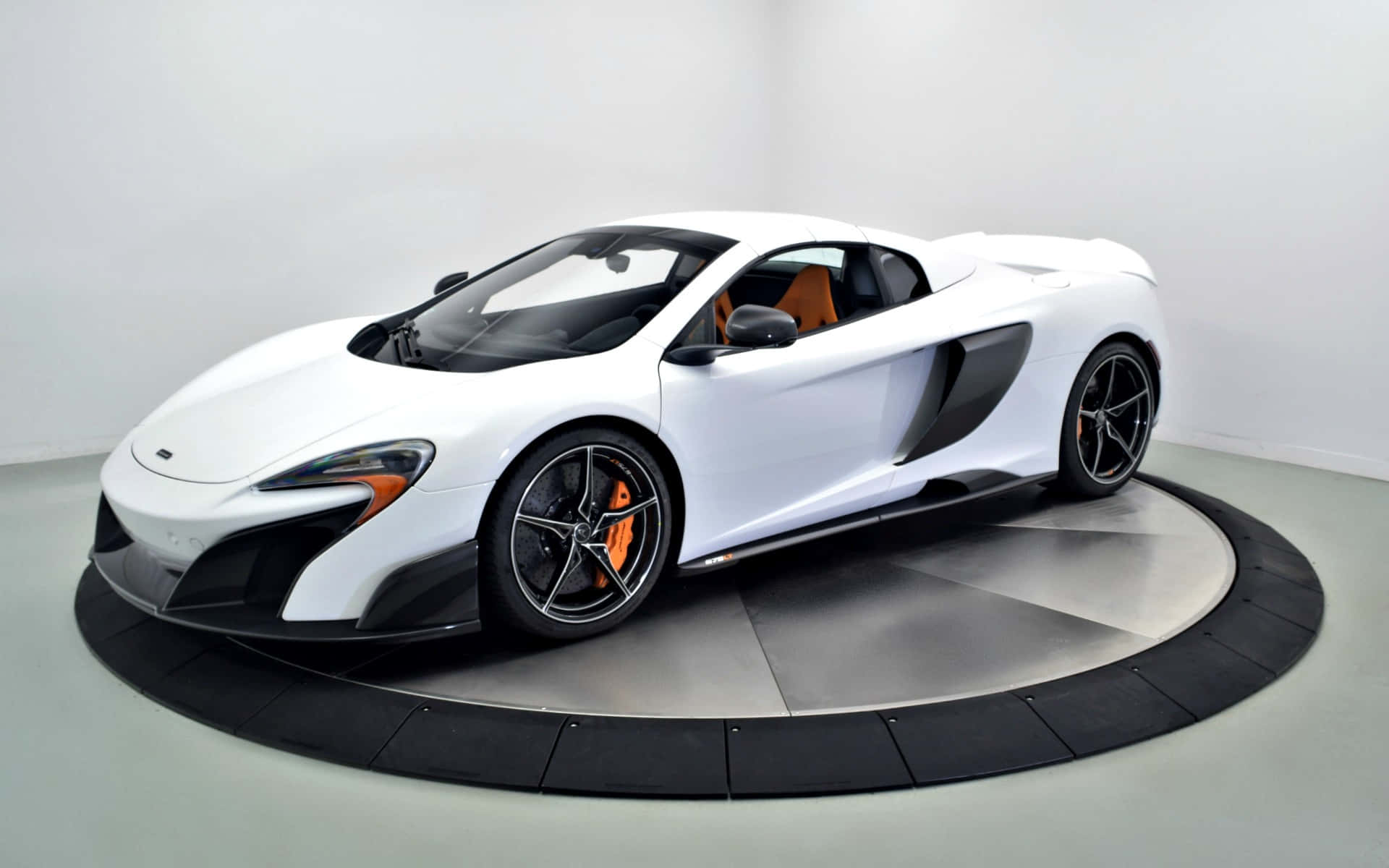 Mclaren 675lt Spider 桌布 壁紙 — 一架時尚的白色McLaren跑車帶有橙色點綴，位於簡約工作室的圓形展示平台中央。