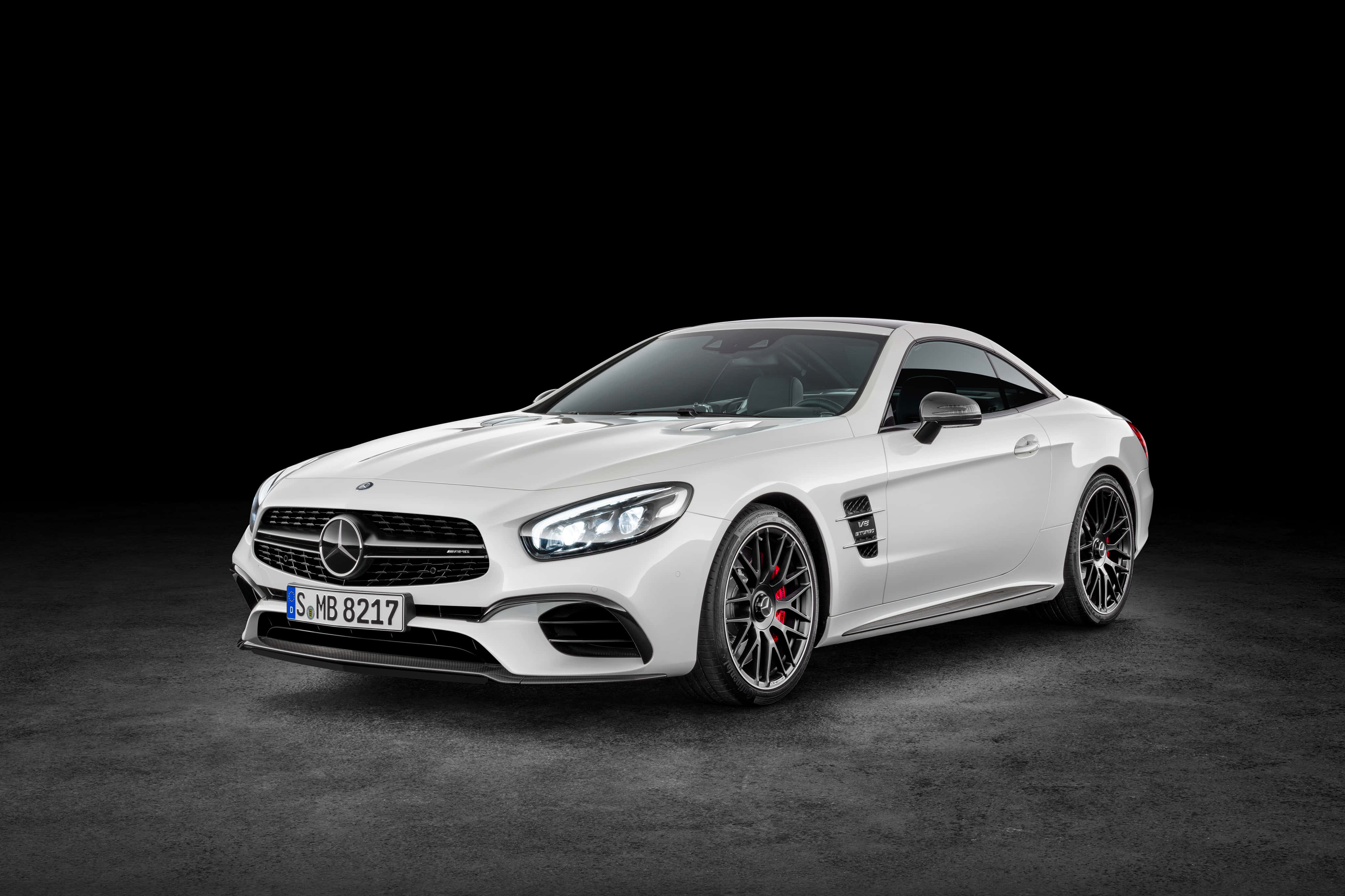 Mercedes Benz Sl-class 桌布 壁紙 — 一架流線型白色 Mercedes-AMG SL63 跑車，配備黑色輪圈和紅色制動卡鉗，在黑色背景的暗色工作室地板上蓄勢待發。