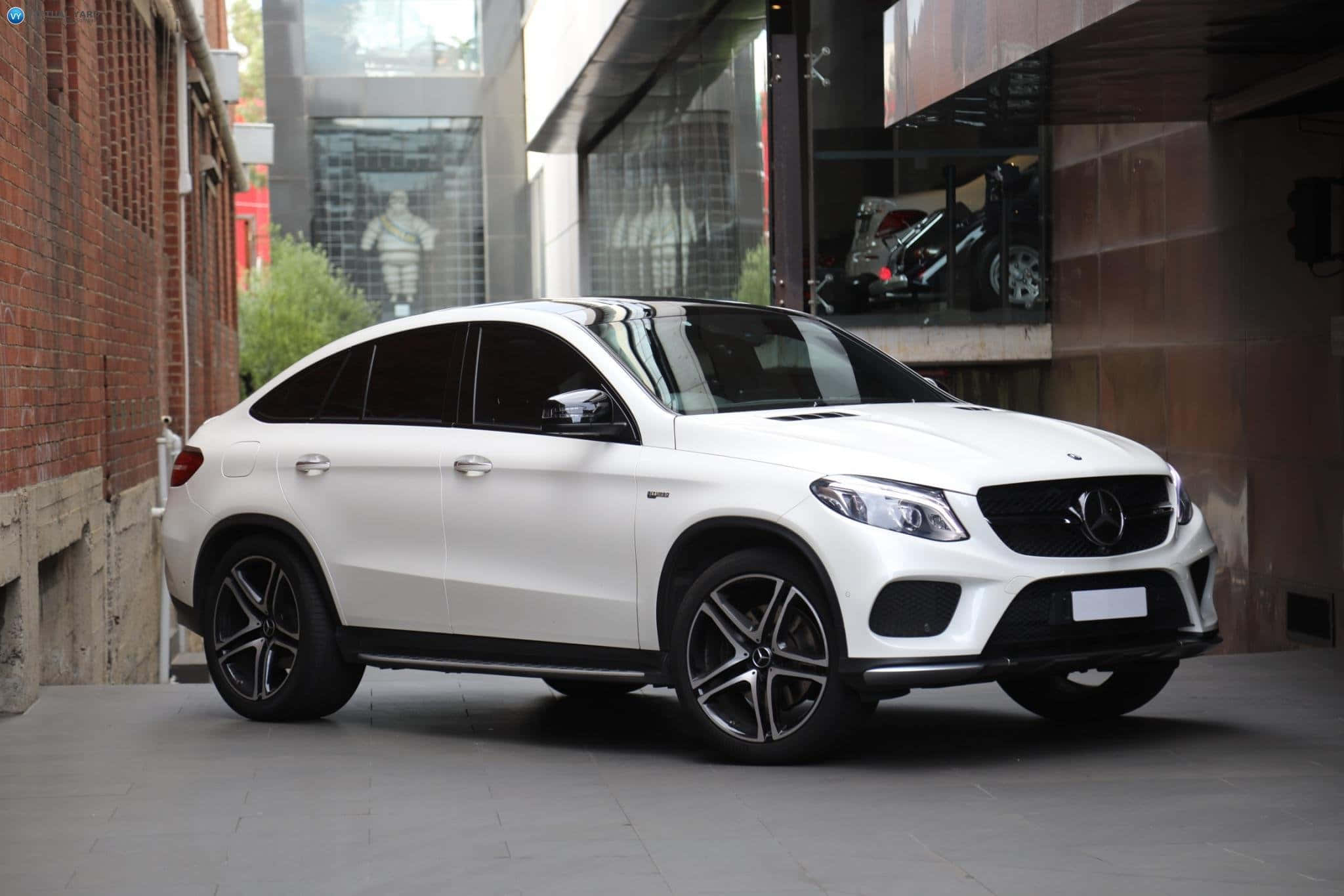 Mercedes Benz Gle-class 桌布 壁紙 — 一輛時尚的白色平治 GLE Coupe 停泊在磚牆和玻璃建築之間的城市小巷中。