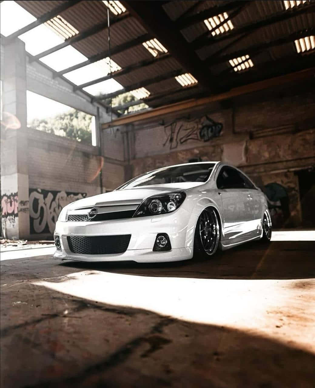 Opel Astra 桌布 壁紙 — 一架時尚的白色改裝轎跑車停放在一個佈滿塗鴉的倉庫內，陽光透過天窗照射進來。