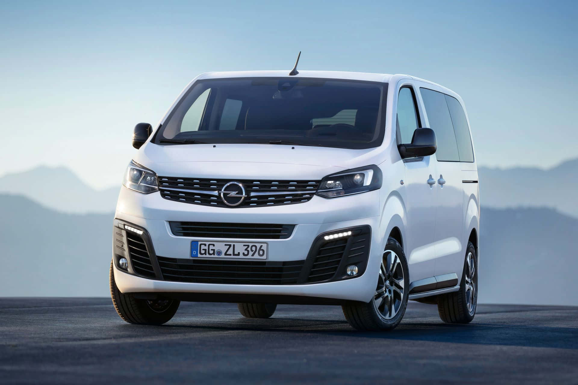 Opel Zafira 桌布 壁紙 — 一架時尚的白色Opel Zafira Tourer客貨車停泊在鋪砌道路上，背景是朦朧的山脈，天空清澈湛藍。
