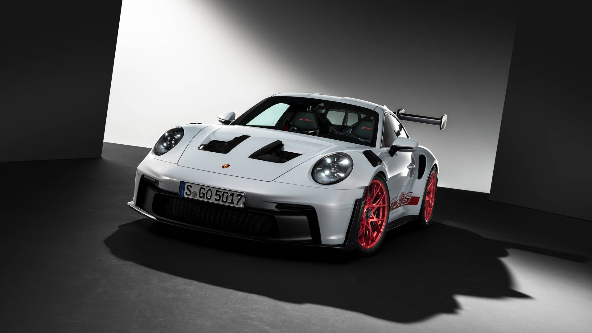 白色保時捷911 GT2 RS配紅色輪圈，在昏暗的攝影棚中由聚光燈照射。