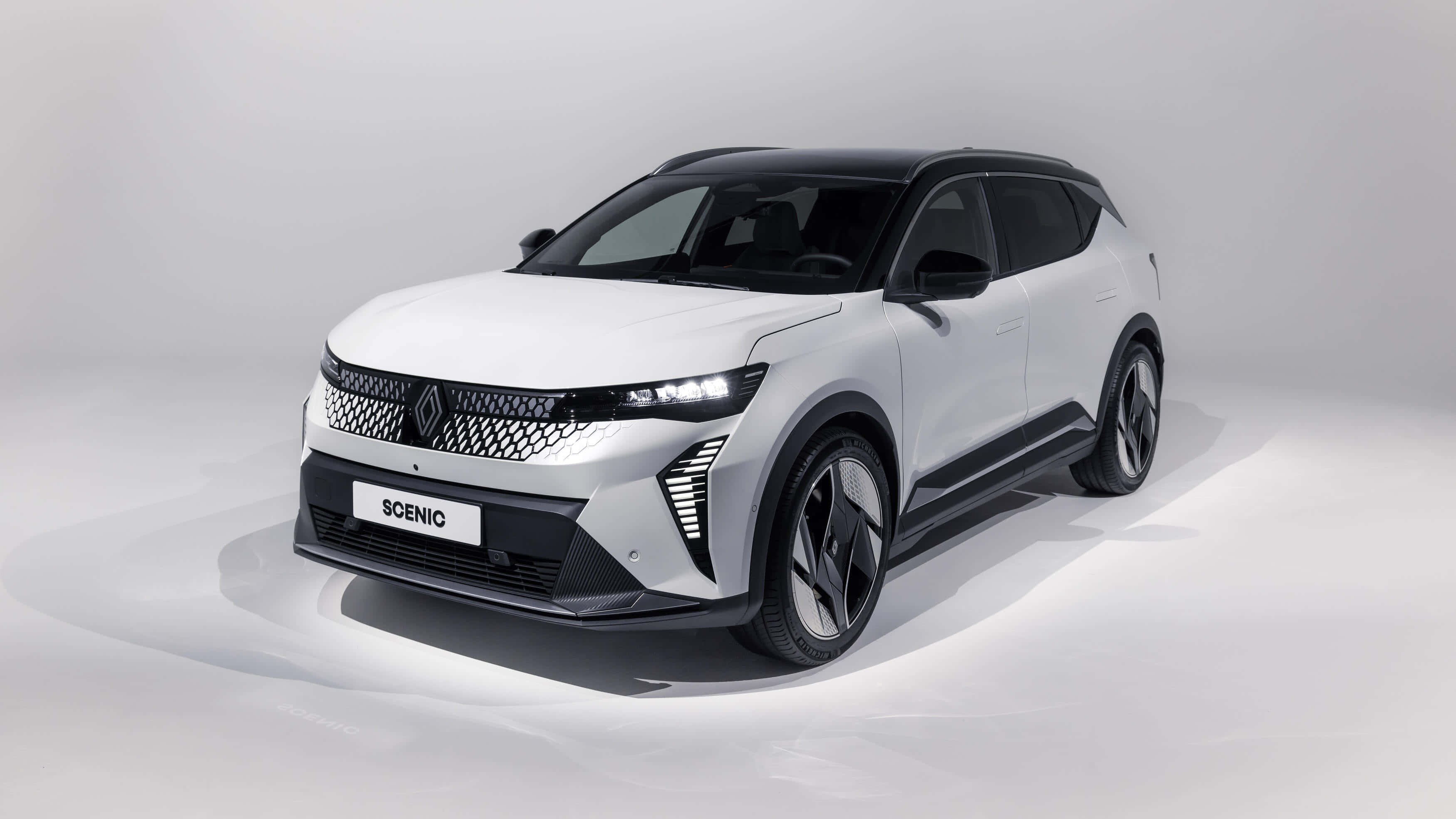 Renault Scenic 桌布 壁紙 — 一部時尚的白色雷諾 Scenic SUV，帶有黑色飾邊和未來感車頭燈，在簡約的攝影棚環境中展示。