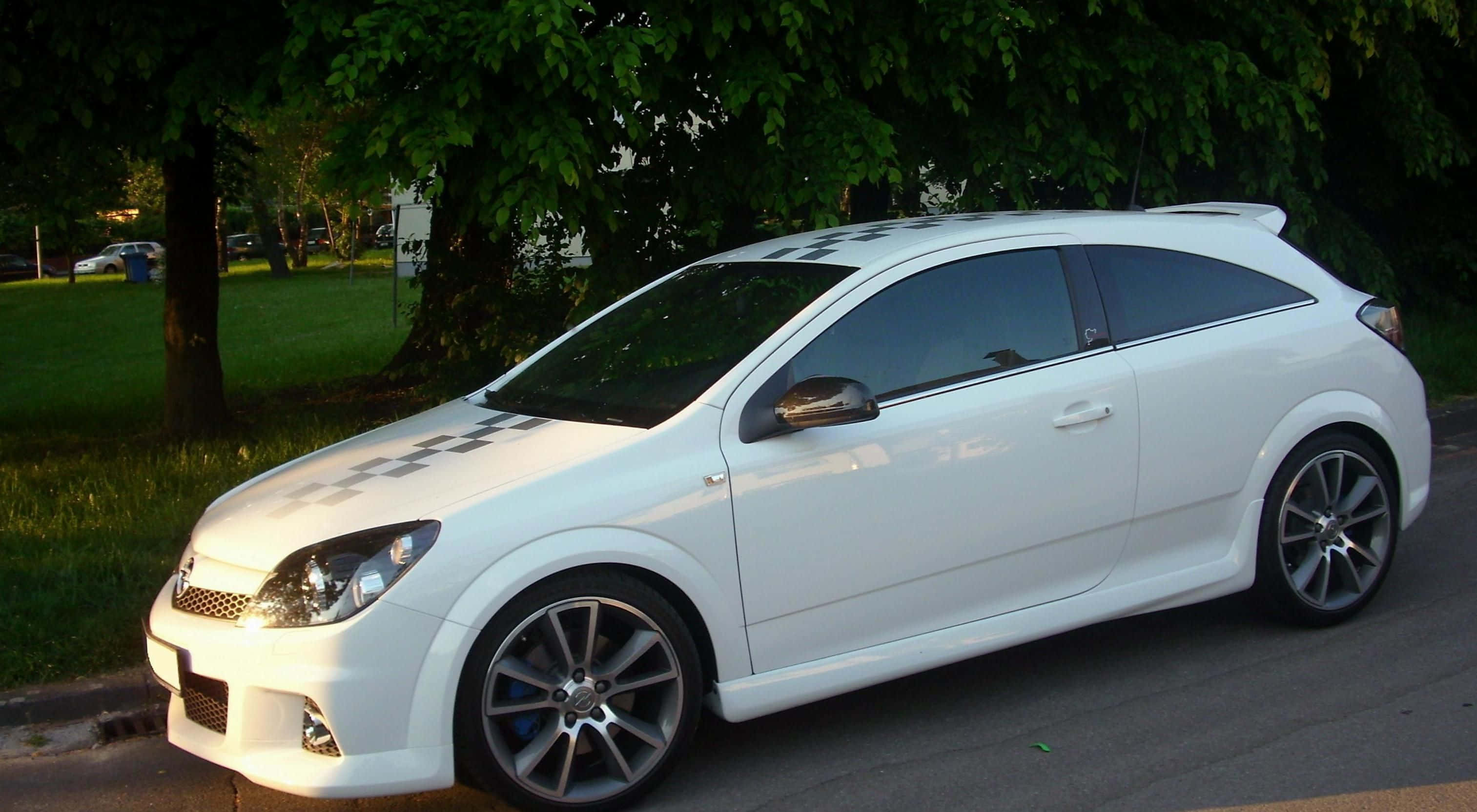 Opel Astra 桌布 壁紙 — 一輛時尚的白色跑車帶有格子圖案貼紙，在黃金時刻停泊在綠樹成蔭的街道上。
