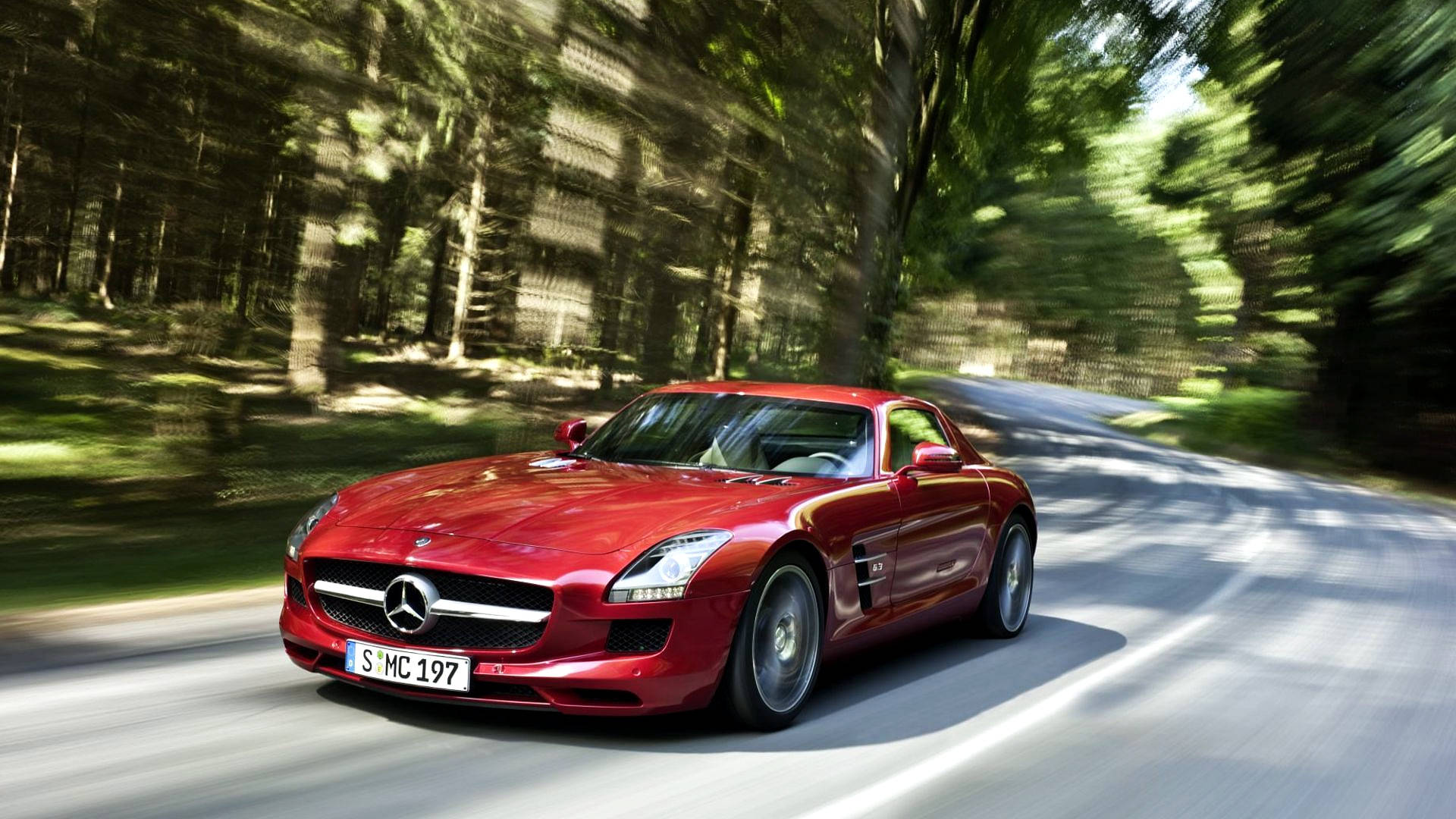 紅色梅賽德斯SLG跑車 壁紙 — 一輛充滿活力的紅色 Mercedes SLS AMG 跑車在蜿蜒的森林道路上疾馳，周圍帶有動態模糊效果。
