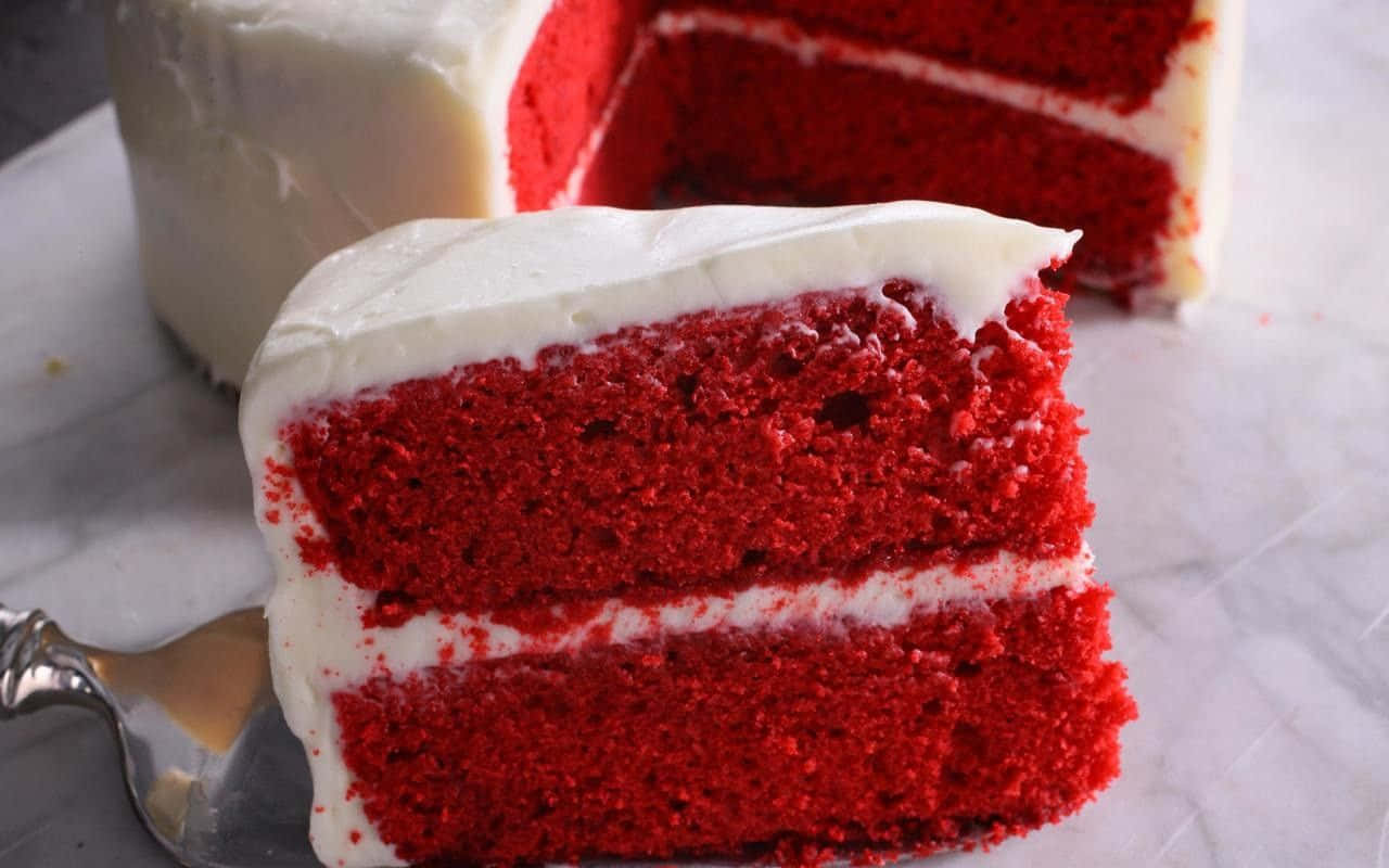 Red Velvet Cake 桌布 壁紙 — 一塊濕潤的紅絲絨蛋糕，配上 creamy 白色糖霜，放在大理石表面上，旁邊有蛋糕鏟。
