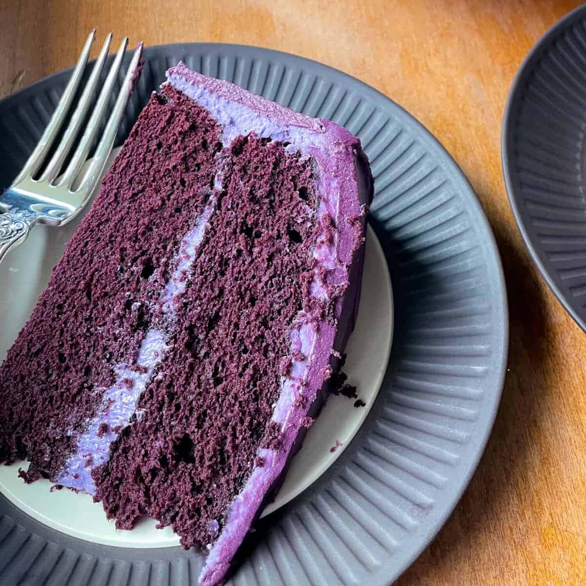 Purple Velvet 桌布 壁紙 — 一片濃郁的紫色天鵝絨蛋糕，配上相配的糖霜，放在灰色有紋的碟子上，旁邊有一把銀叉。