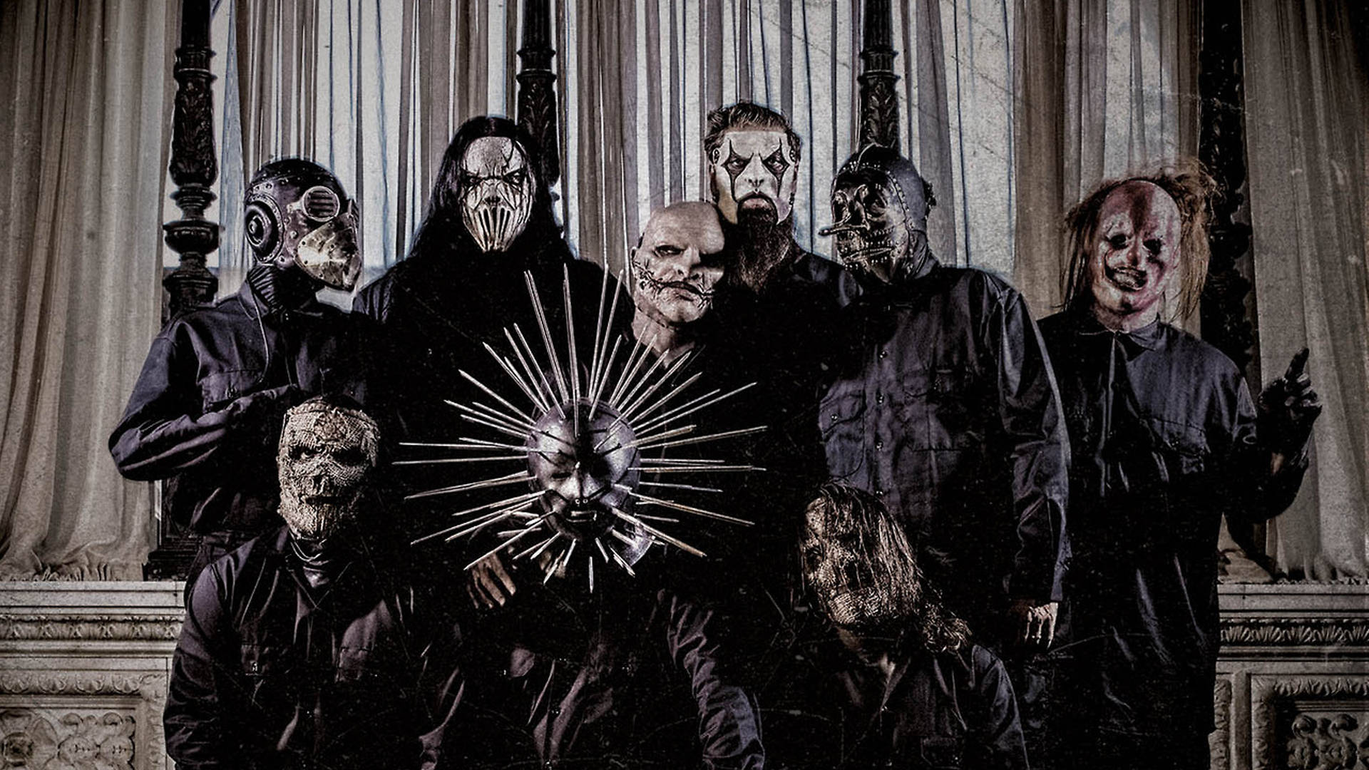 Slipknot 成員與克雷格·瓊斯 壁紙 — 一群戴著面具、身穿深色衣服的人物在一個哥德式房間裡擺出威脅性的姿勢，房間裡有華麗的窗簾和一個帶尖刺的太陽爆發面具作為中心裝飾。