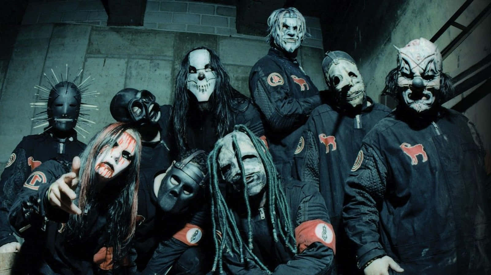 Slipknot - 桌面壁紙 壁紙 — 一群戴著面具、身穿深色制服的音樂人在粗糙的混凝土走廊中強烈地擺姿勢。