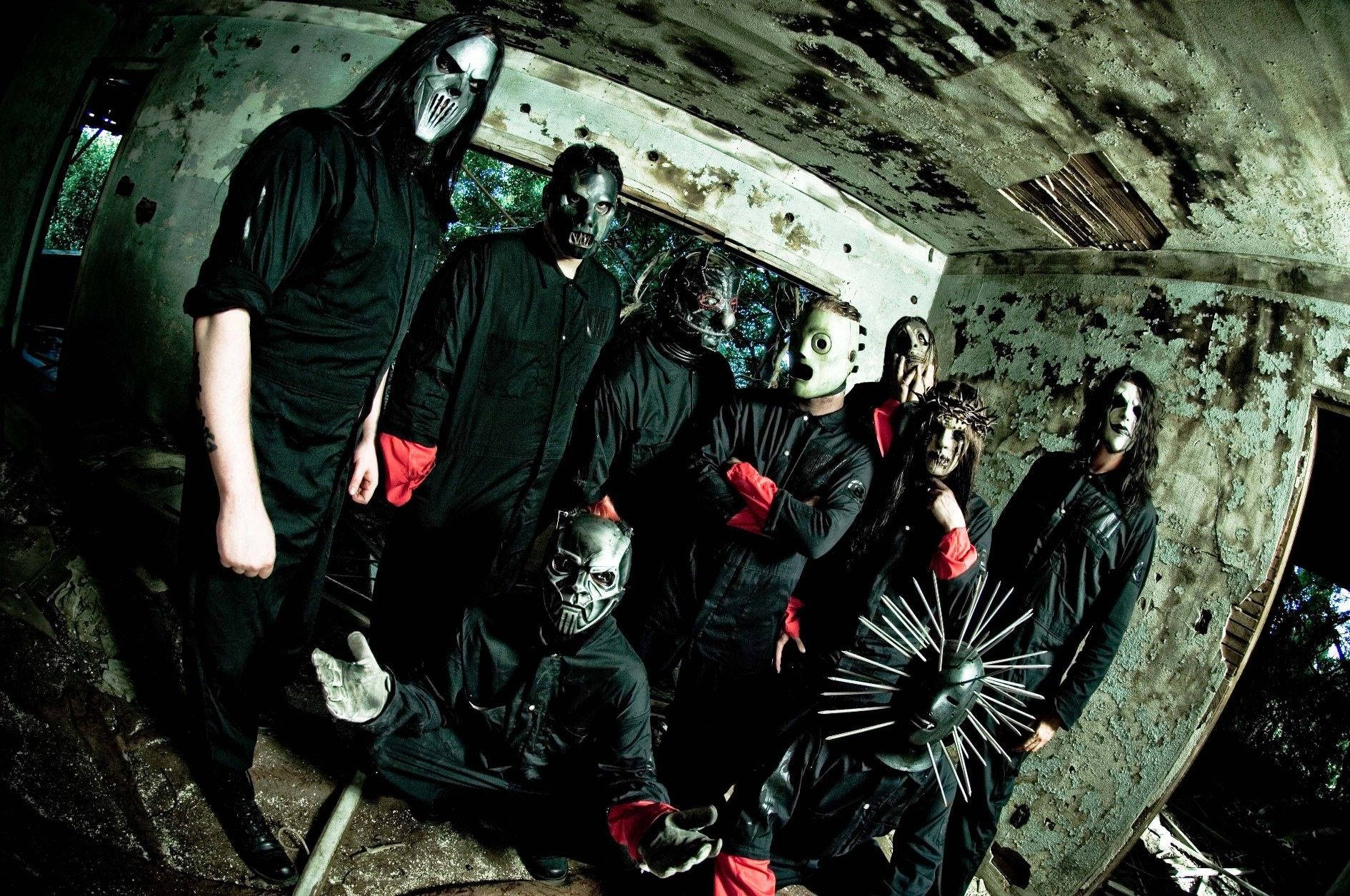 Slipknot 樂團帶魚眼效果 壁紙 — 一個穿著黑色服裝和怪誕面具的樂隊在腐朽的混凝土結構內擺出威脅性的姿勢。