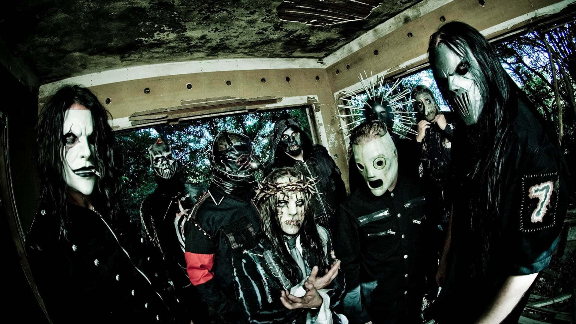 Slipknot桌面壁紙 壁紙 — 一群戴著面具、身穿黑色服裝的音樂人在一個佈滿青苔、窗戶破損的破舊房間內擺出威脅姿勢。