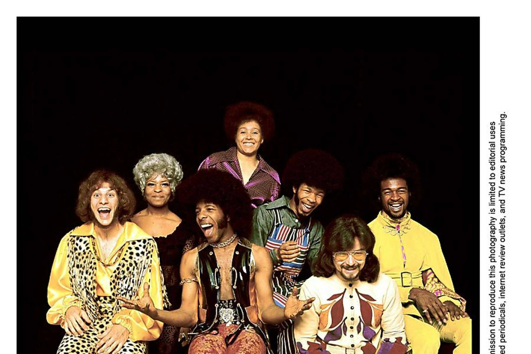 Sly 及 The Family Stone 成員拍攝 壁紙 — 七位快樂的1970年代音樂家，留著非洲式髮型，穿著大膽圖案的服裝，在黑色背景前擺姿勢。