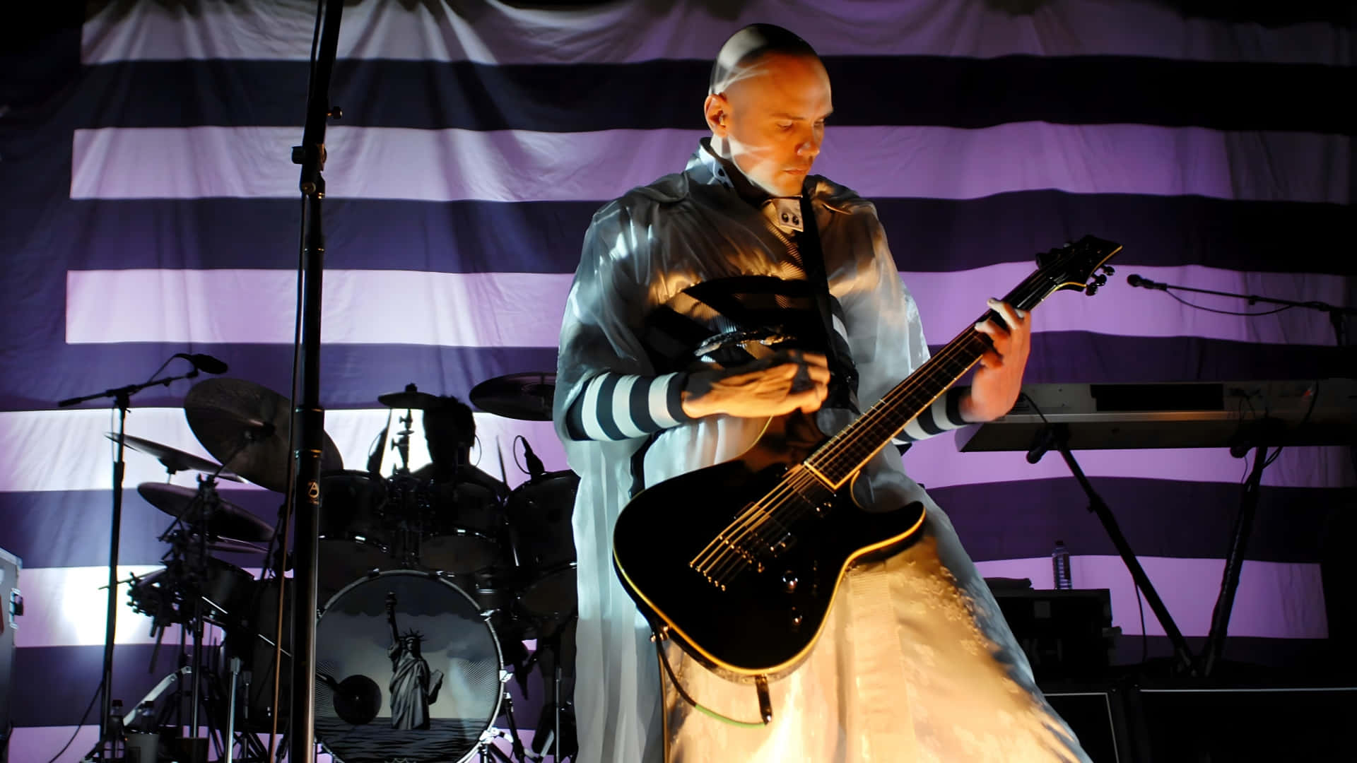 Smashing Pumpkins 演唱會現場 壁紙 — 一位身穿閃亮銀色長袍的音樂家在紫色舞台燈光下，以條紋背景彈奏黑色電結他。