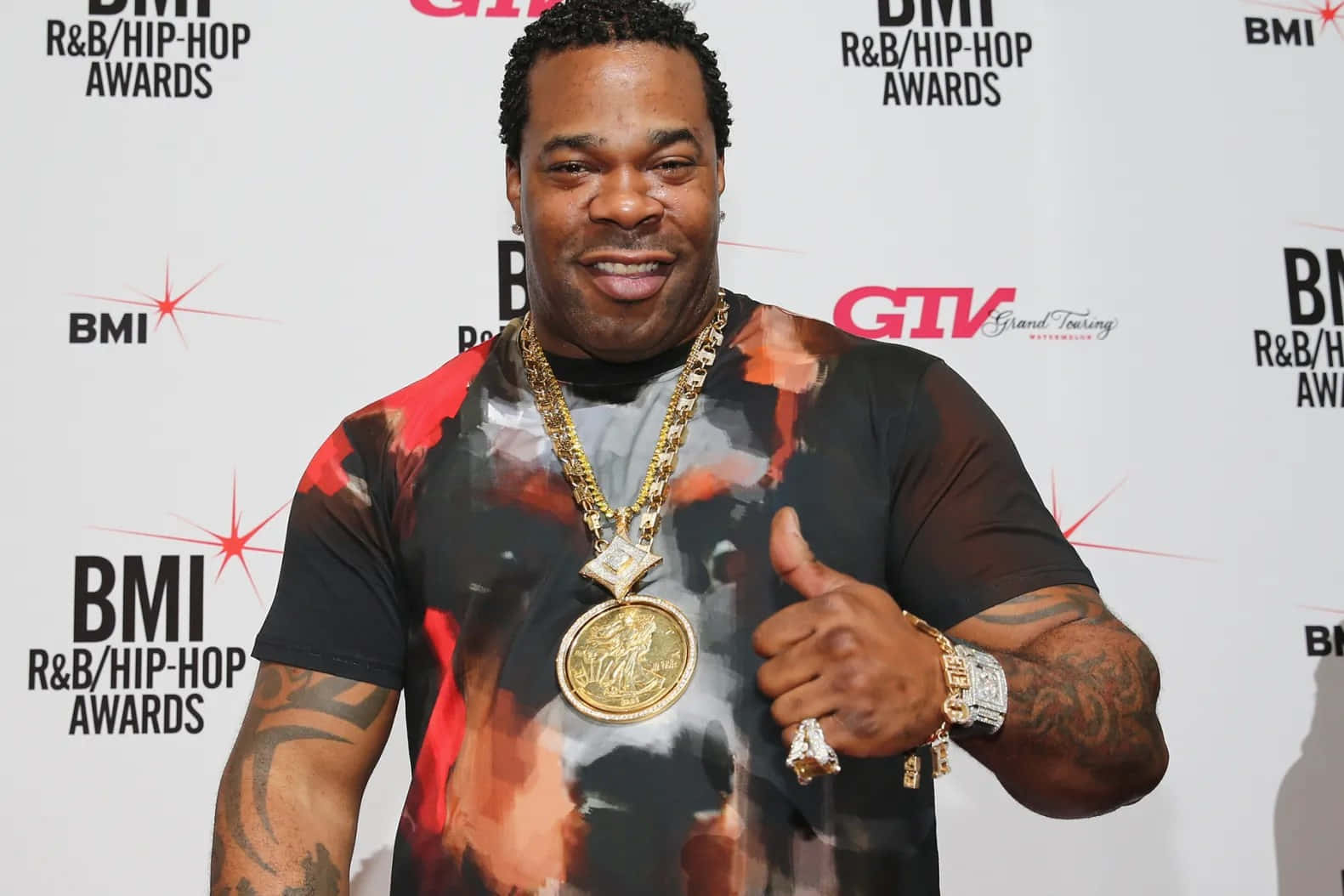  壁紙 — 一位面帶微笑的男子穿著圖案T恤和厚重金鏈，在BMI R&B/Hip-Hop Awards紅地毯上豎起大拇指。