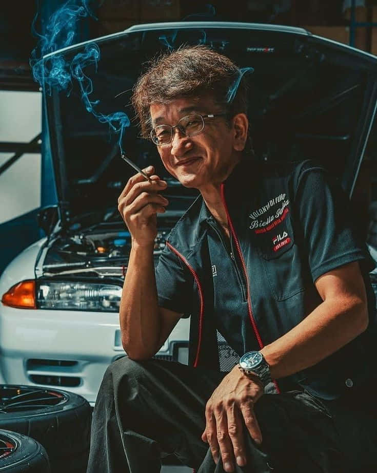 Smokey Nagata修車後照片 壁紙 — 車房裏一位微笑的機械師，坐在一輛打開引擎蓋的白色汽車前抽煙。