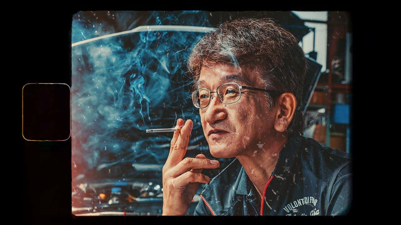 Smokey Nagata手機螢幕影像 壁紙 — 一位戴眼鏡的較年長男性在模糊的城市背景下吸煙，藍色煙霧在他周圍旋轉。