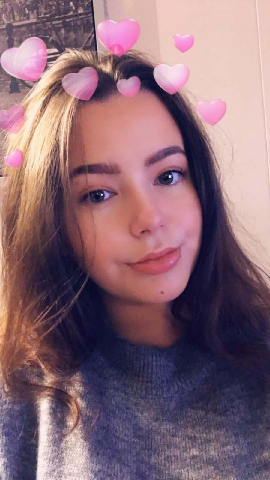 Snapchat 粉紅心形頭部濾鏡照片 壁紙 — 一位年輕女性留著長長棕色頭髮，在自拍中微笑，粉紅色心形表情符號漂浮在她頭部周圍。