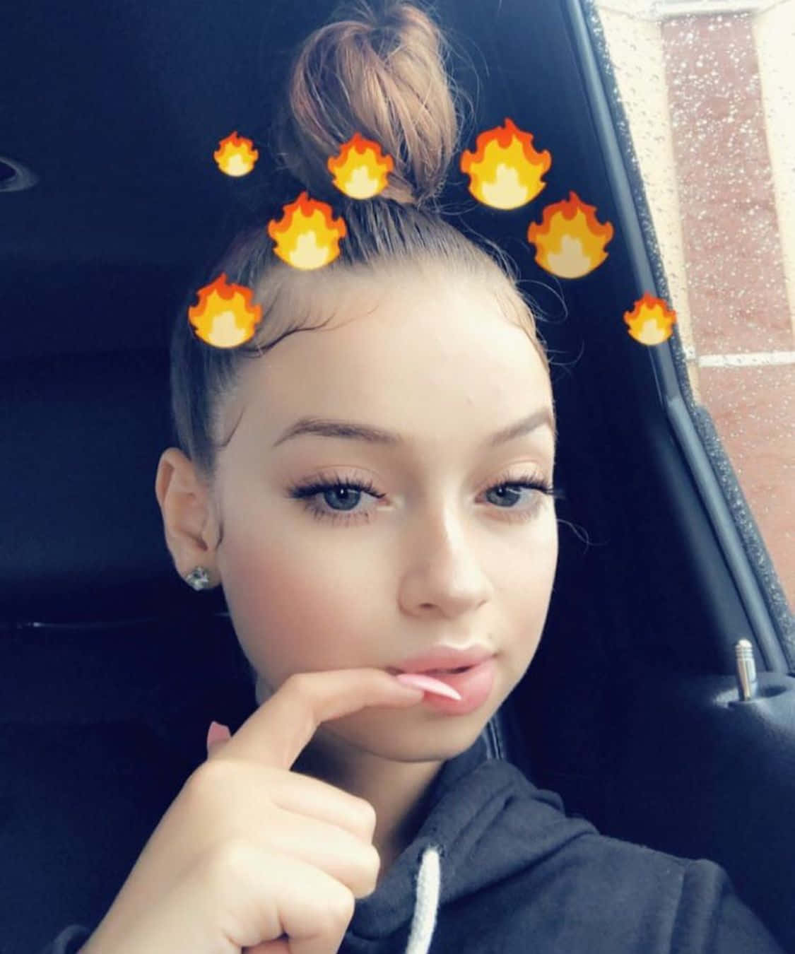 年輕女性在髮髻上帶有火焰表情符號，在車內自拍。