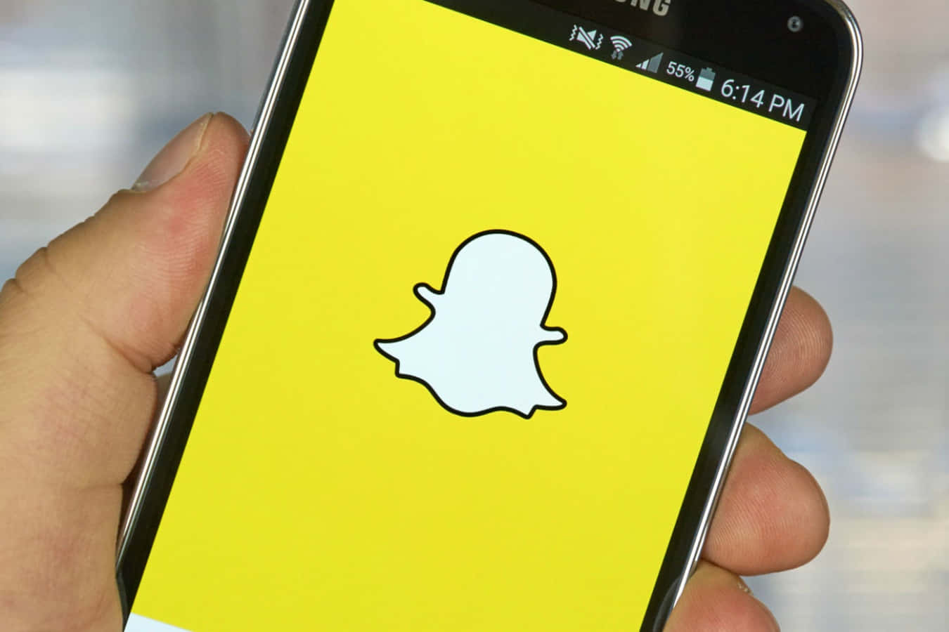 手拿智能手機，黃色屏幕上顯示Snapchat應用程式標誌。