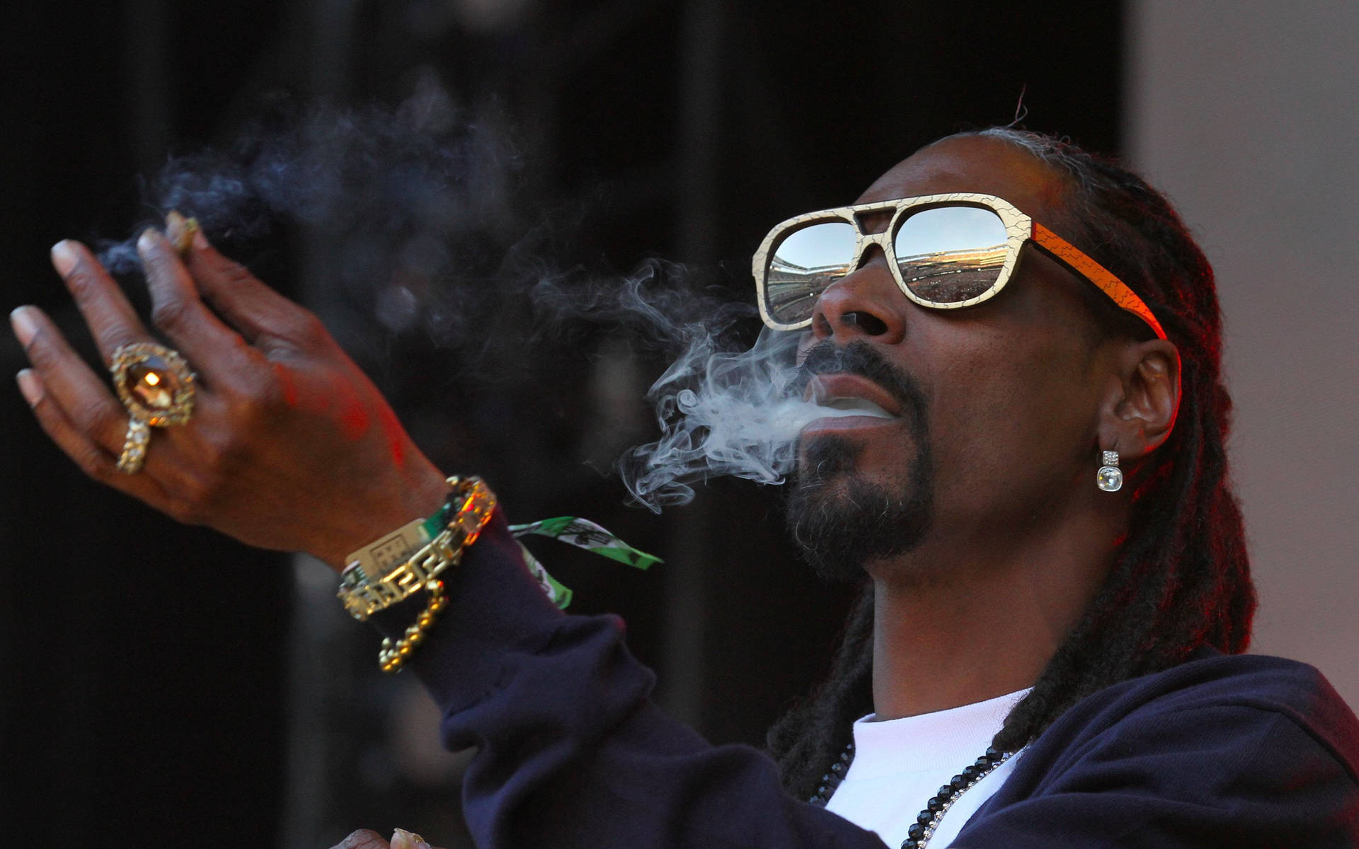 Snoop Dogg 戴著金色太陽眼鏡和珠寶呼出煙霧。