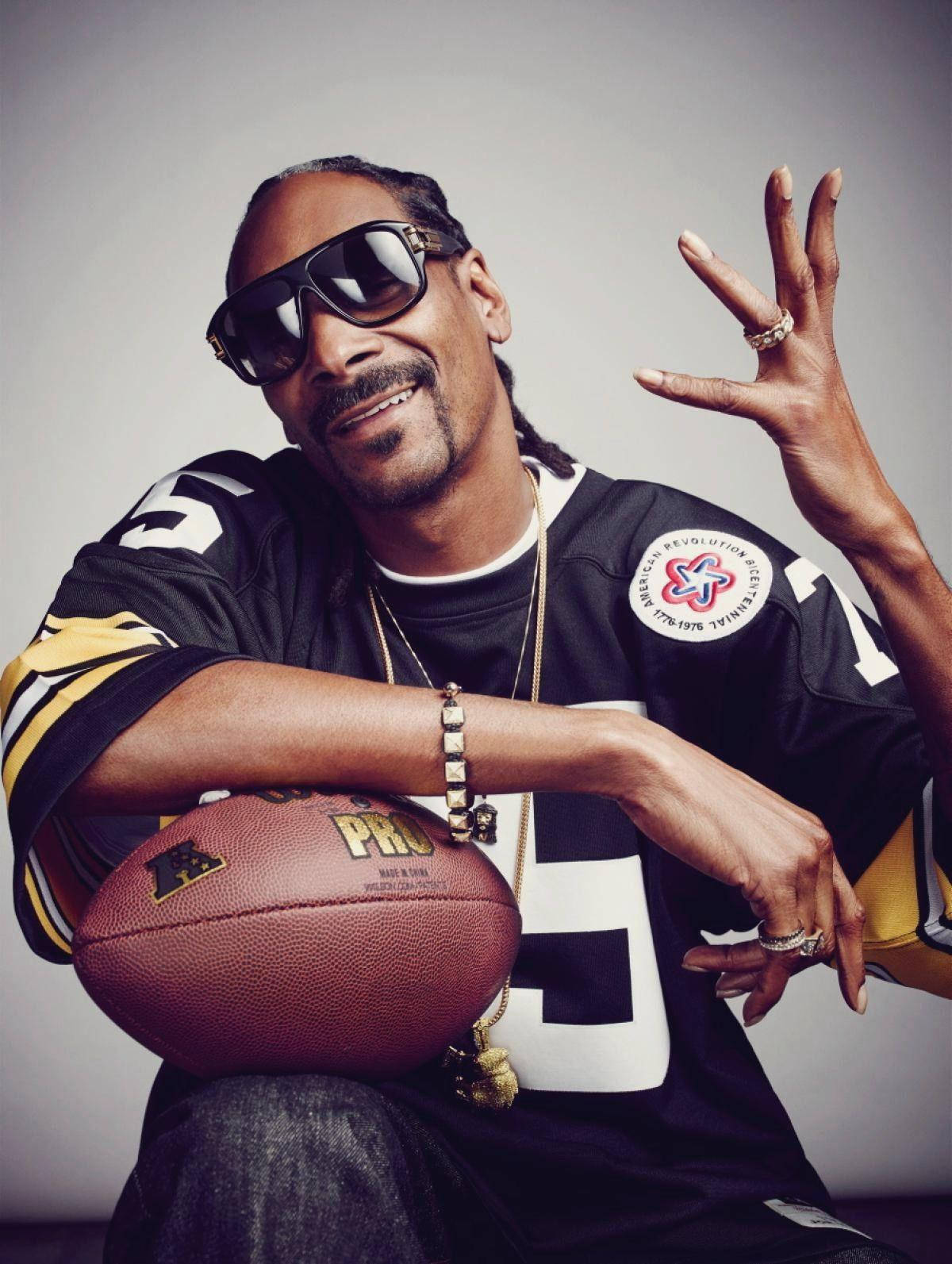 Snoop Dogg 身穿美式足球球衣，手持足球並揮手。