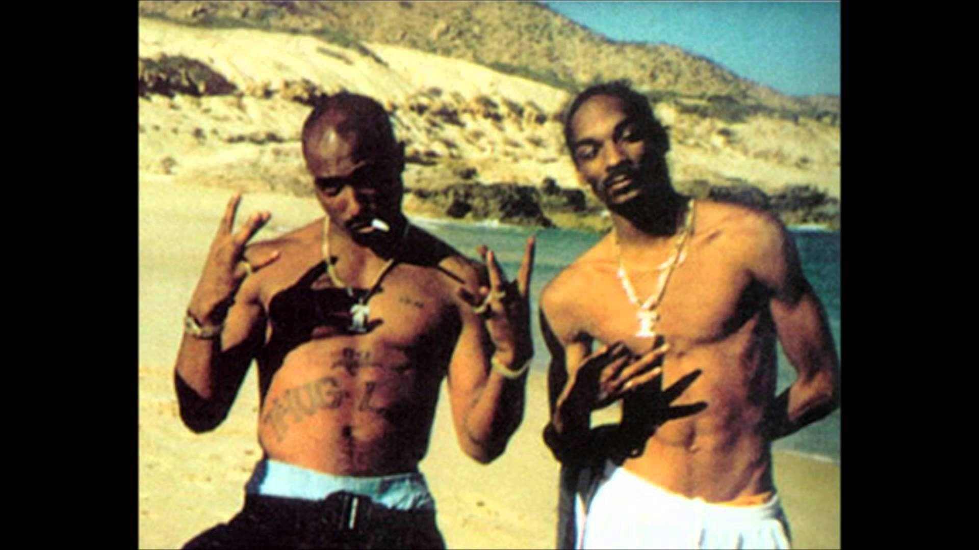 Snoop Dogg 與 2Pac 壁紙 — 兩名赤裸上身的男子在陽光明媚的海灘上擺姿勢，身後是岩石丘陵，兩人都做出手勢。