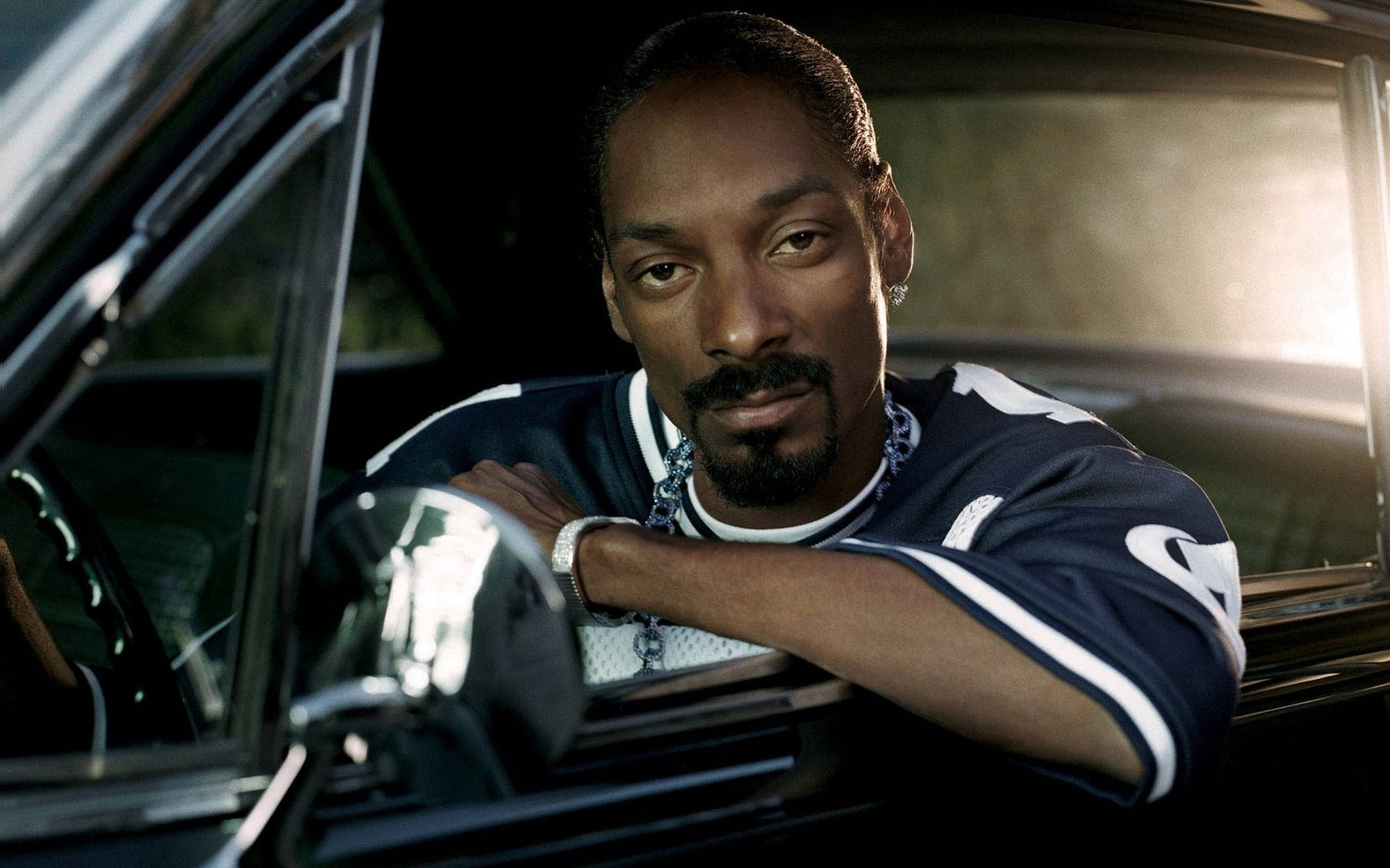 Snoop Dogg 車內悠閒 壁紙 — Snoop Dogg 從一輛浸浴在金色背光中的復古車窗中酷酷地探出頭來。