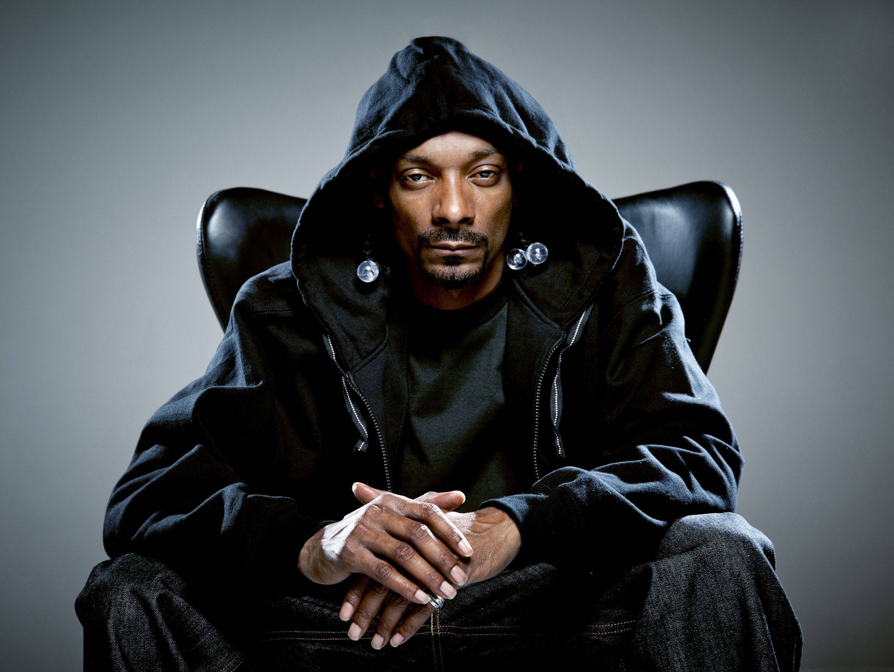 Snoop Dogg 黑色皮革椅 壁紙 — Snoop Dogg 冷靜地坐在黑色皮椅上，身穿黑色連帽衫，戴著銀色耳環，手部纏著繃帶。