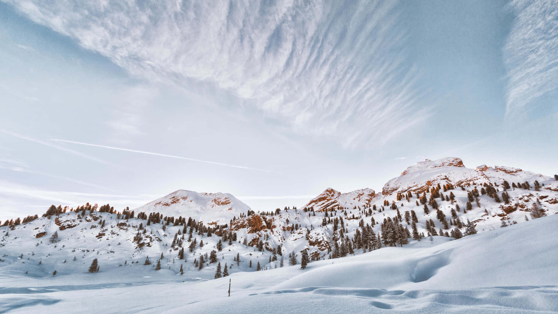  壁紙 — 白雪覆蓋崎嶇的山峰，天空點綴著纖細的卷雲和隱約的飛機雲。