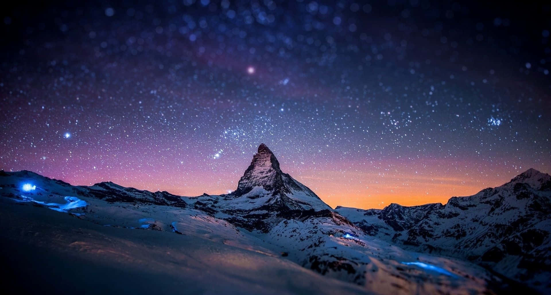 在紫色和橙色色調的星空暮色天空下，白雪覆蓋的山峰。