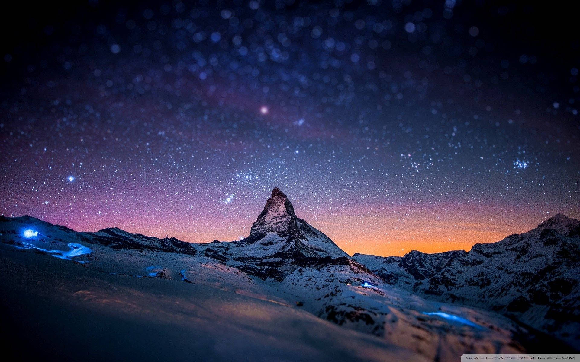 白雪覆蓋的山峰在紫色和橙色色調的星空暮色天空下。