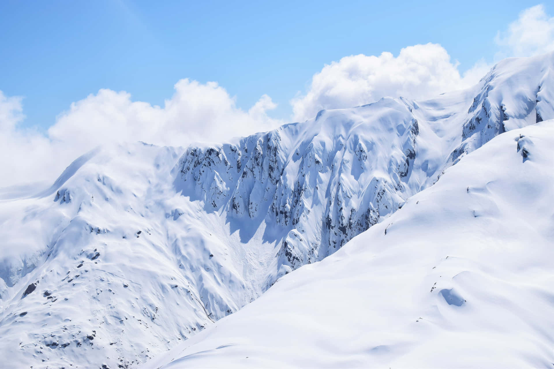 晴朗藍天與零星白雲下的雪山山脈。