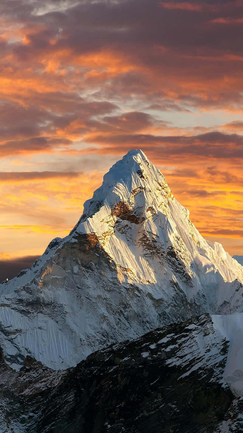  壁紙 — 白雪覆蓋的山峰在火紅的夕陽天空下閃耀著金色光芒，天空中有橙色和紫色的條紋雲彩。