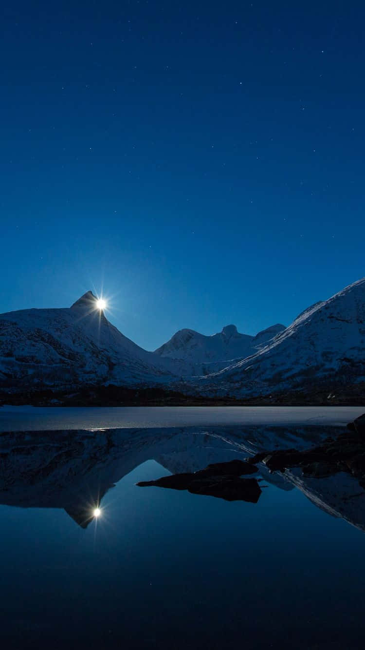  壁紙 — 積雪的山峰在明亮的月亮下閃耀，在平靜、繁星點點的夜湖中投射出完美的倒影。