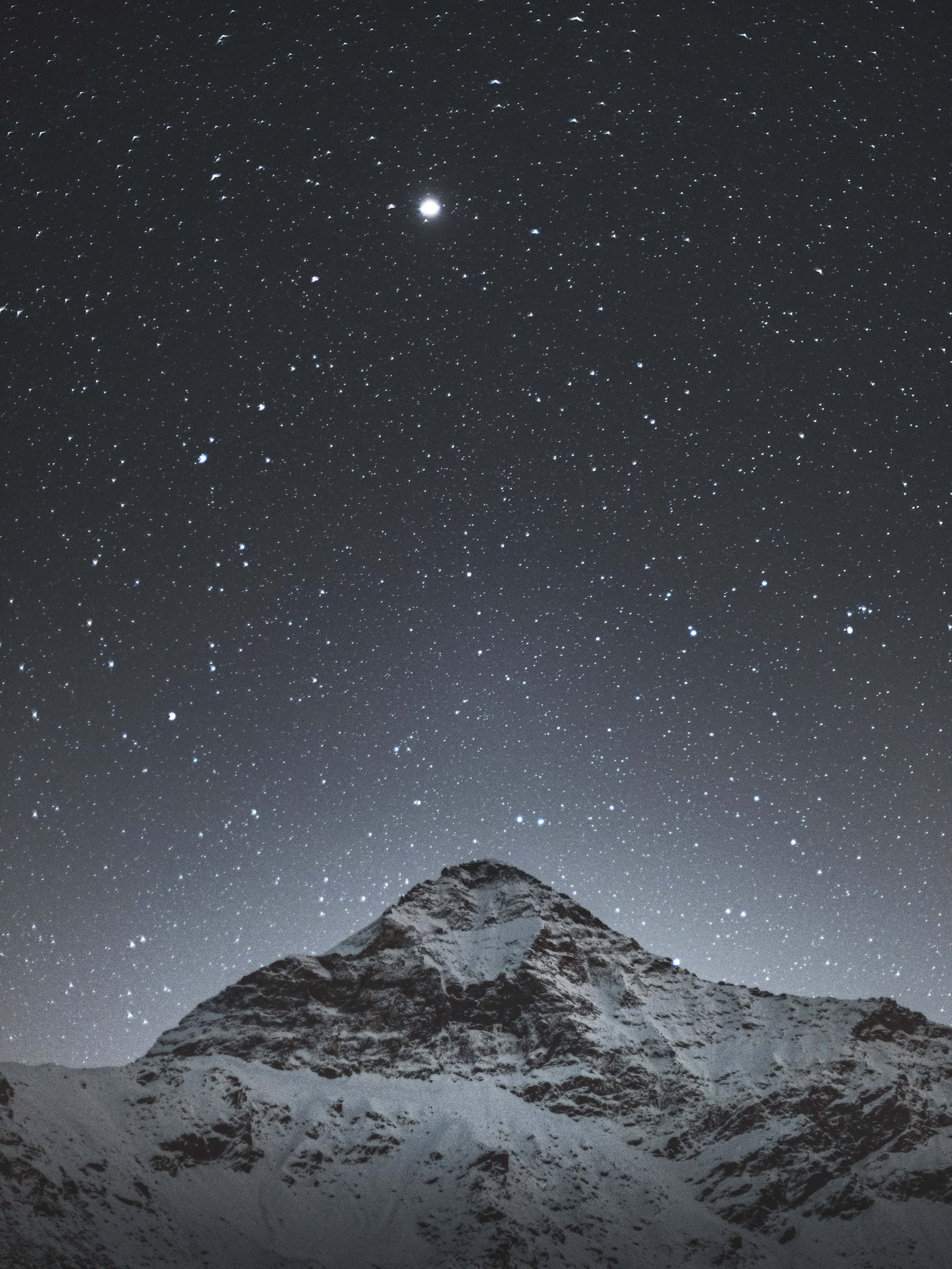 shining 桌布 壁紙 — 白雪覆蓋的山峰在繁星點點的夜空下升起，上方有一顆明亮的天體發光。
