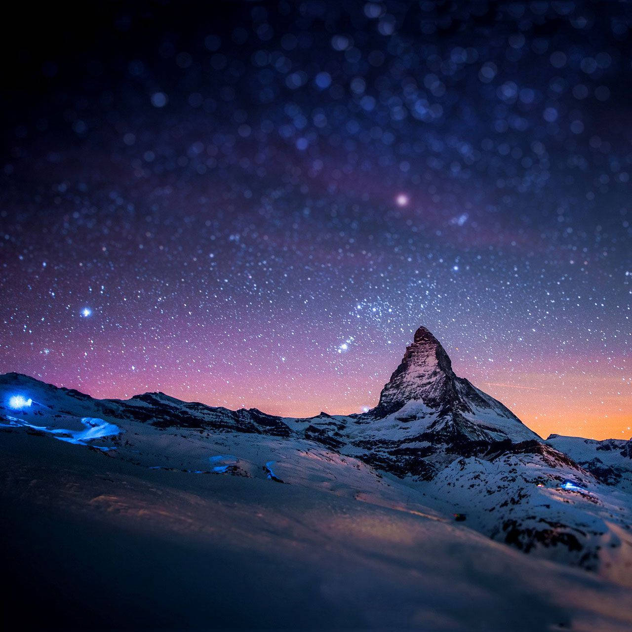 星空下的山巔 Samsung Galaxy 平板 壁紙 — 白雪覆蓋嘅馬特洪峰喺星光燦爛嘅暮色天空下聳立，帶有紫色同橙色色調，山坡上仲有發光嘅藍色燈光。