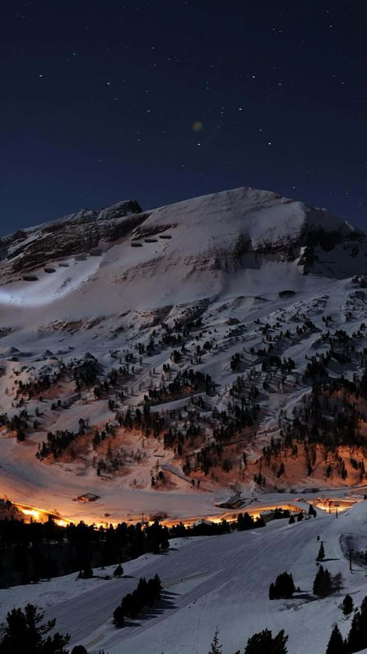 壁紙 — 白雪覆蓋的山峰，在星空下，溫暖的山谷燈光在下方。
