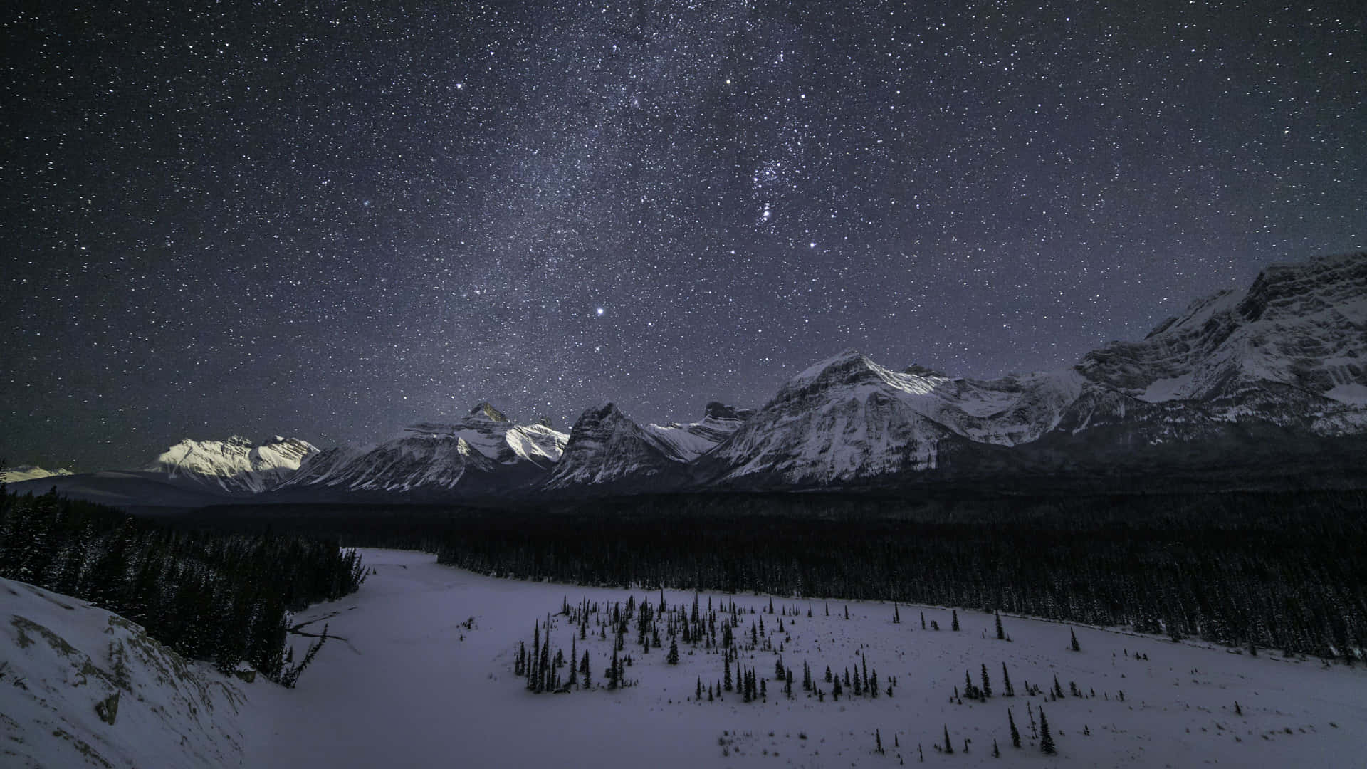  壁紙 — 白雪覆蓋的山峰，在繁星點點的夜空下，一條冰封的河流蜿蜒穿過森林覆蓋的山谷。