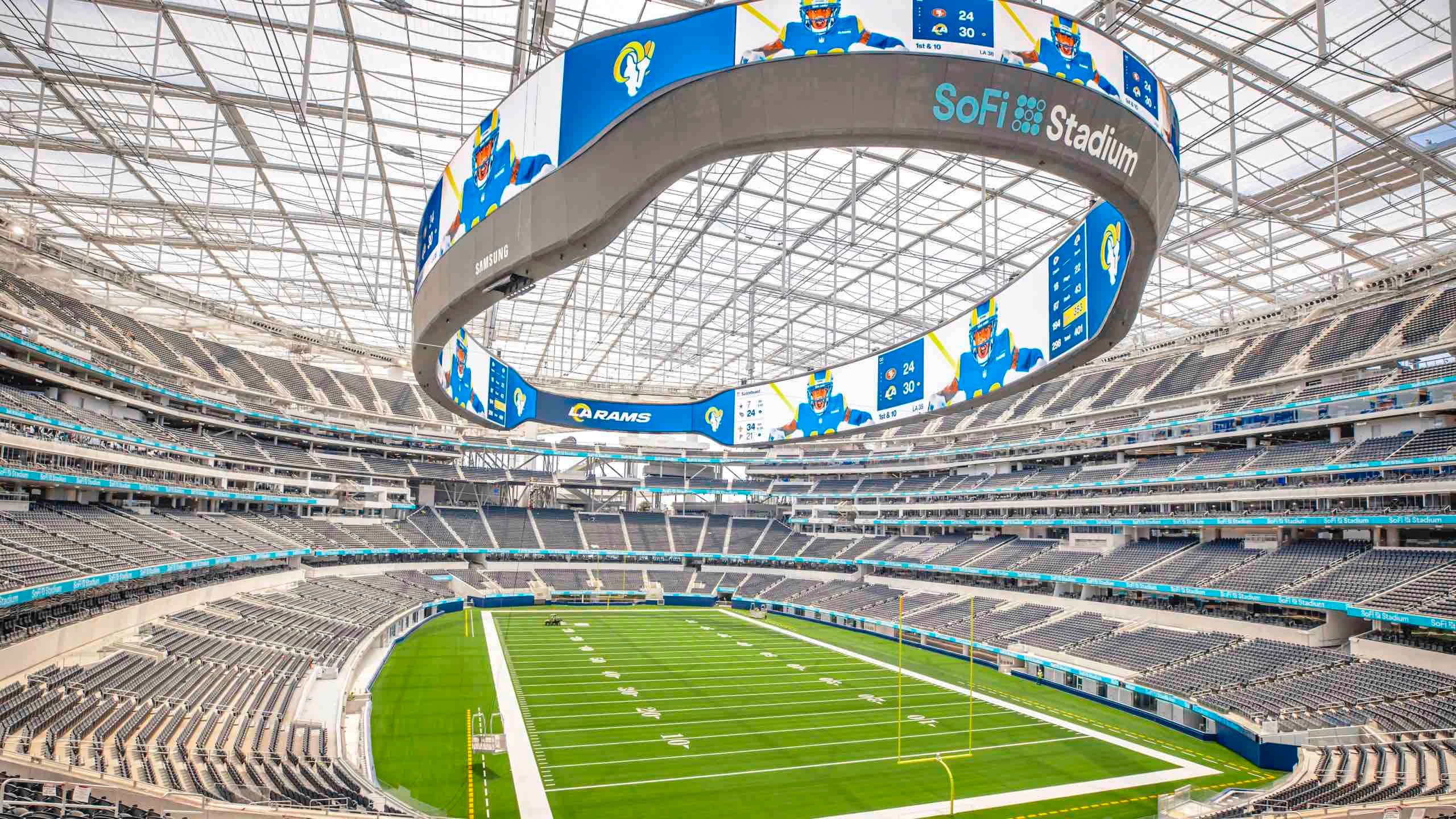 SoFi Stadium，南加州所有體育迷的頂級目的地 壁紙 — 空蕩蕩的SoFi體育場的鳥瞰圖，展示了其巨大的弧形視頻板和玻璃屋頂下充滿活力的綠色足球場。