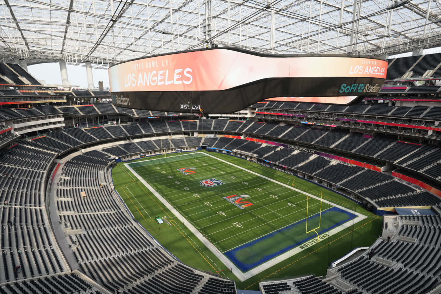 SoFi Stadium外觀航拍，洛杉磯公羊隊與突襲者隊的家 壁紙 — 玻璃屋頂下空無一人的NFL體育場，擁有綠色草坪和黑色座椅的鳥瞰圖。