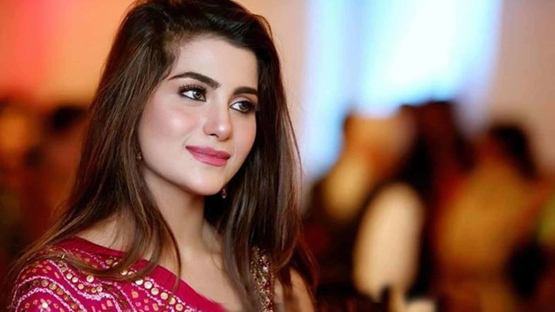 巴基斯坦女星Sohai Ali Abro 壁紙 — 一位身穿紅色裝飾上衣的女性在模糊的派對背景下溫柔微笑。